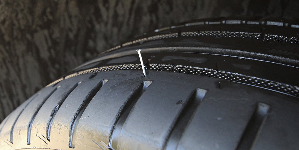 This image shows a car tyre with a nail in the tread